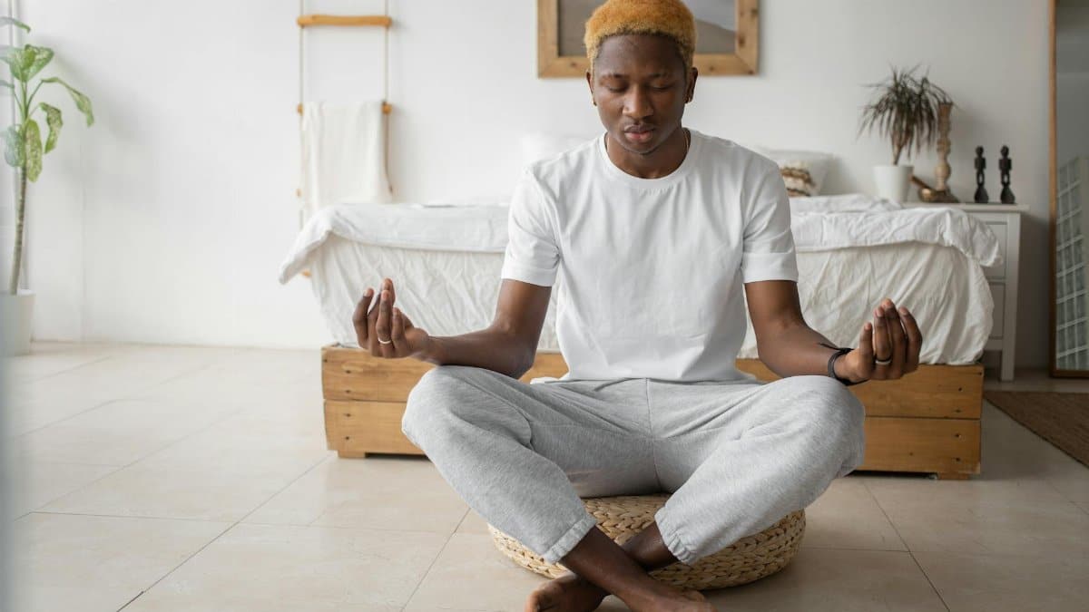 A young man practicing mindfulness meditation in a serene bedroom setting.
