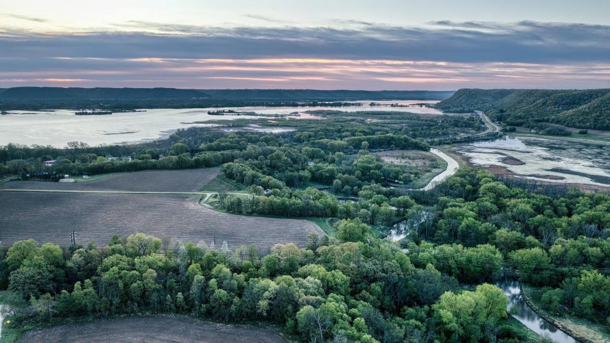 Drone view of lush Minnesota farmland and river landscape at sunset. Ideal for nature and travel themes.