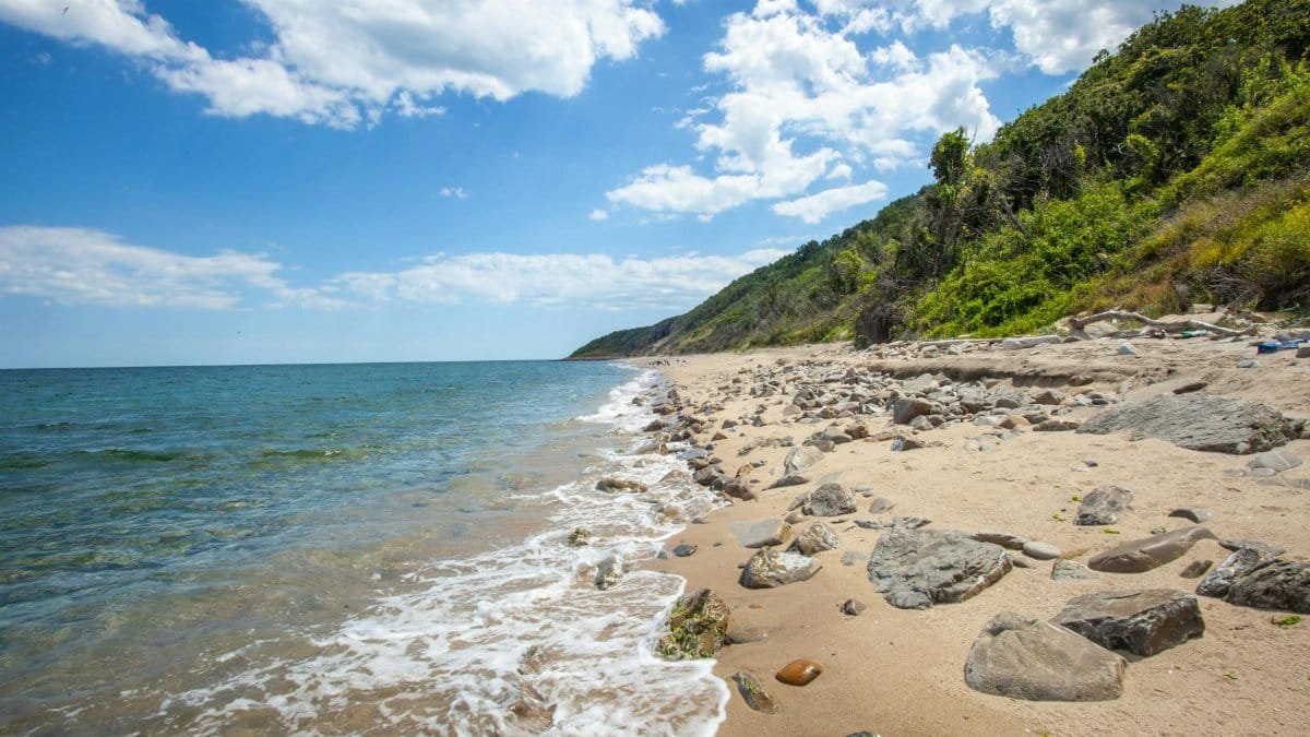 A tranquil rocky beach with waves under a bright summer sky, perfect for coastal relaxation.