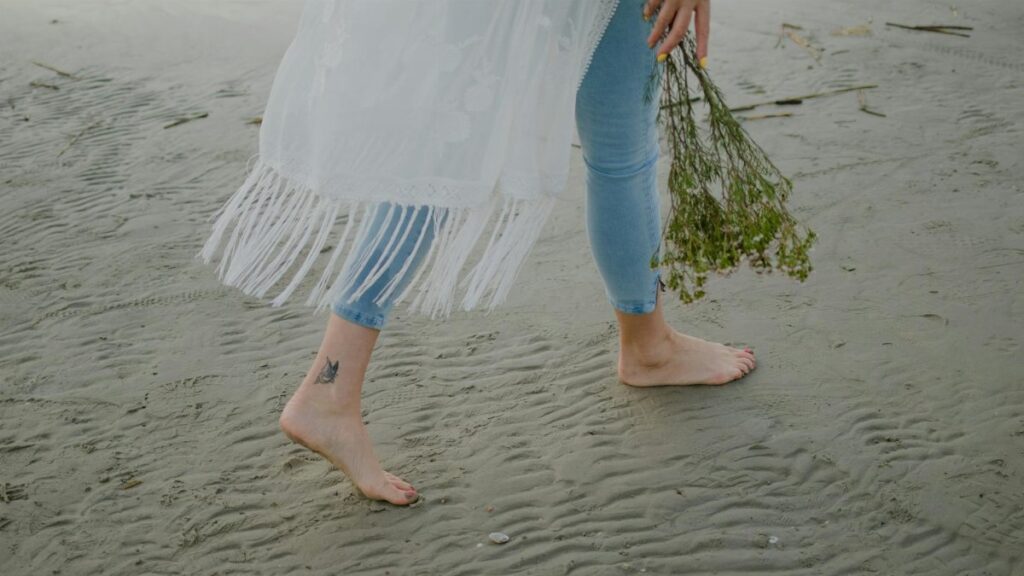 A person walking barefoot on the beach holding a bouquet of wildflowers.