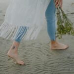 A person walking barefoot on the beach holding a bouquet of wildflowers.