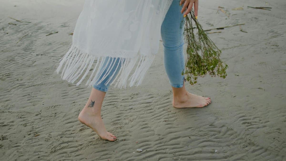 A person walking barefoot on the beach holding a bouquet of wildflowers.
