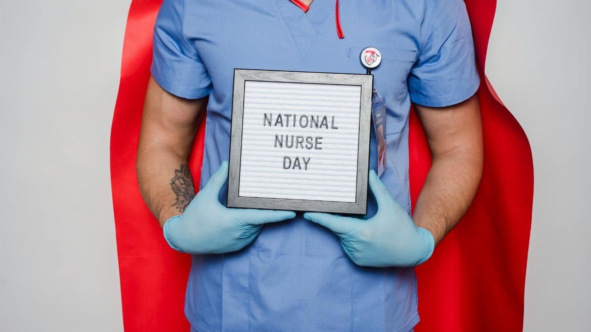 Crop unrecognizable man doctor in blue uniform and red cape demonstrating letterboard with National nurse day inscription against light background
