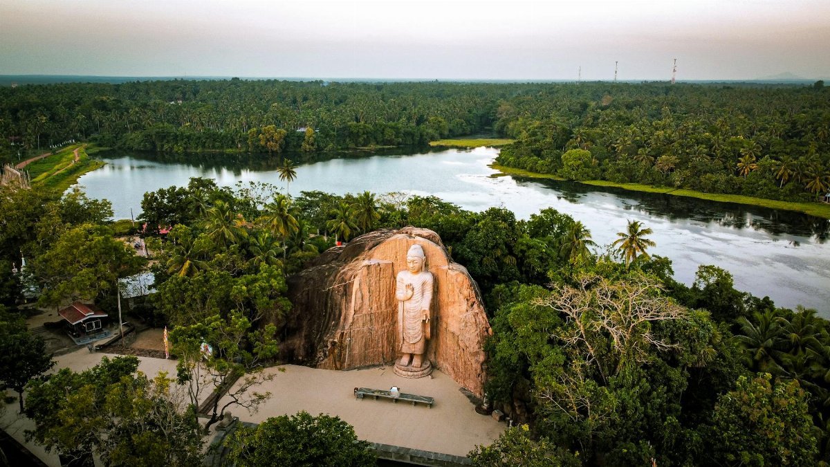 Aerial photograph showcasing the serene Avukana Buddha statue surrounded by lush greenery and a calm river in Sri Lanka.