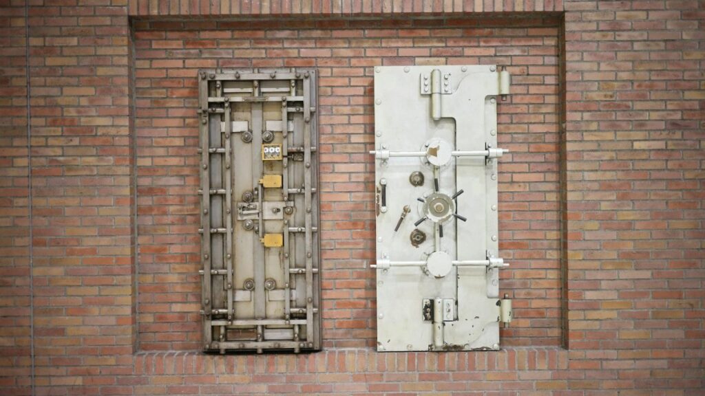 Two steel security vault doors attached to a vintage brick wall, showcasing industrial strength.