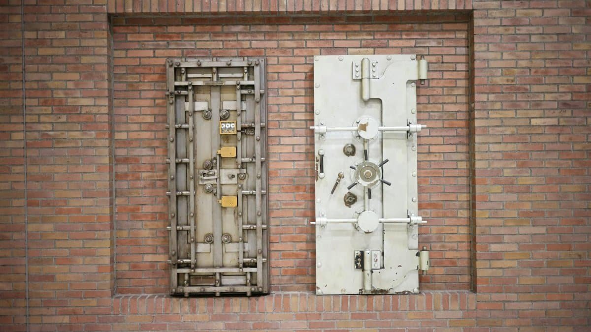 Two steel security vault doors attached to a vintage brick wall, showcasing industrial strength.