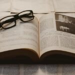 A vintage book open on a table, surrounded by old papers, with resting glasses.