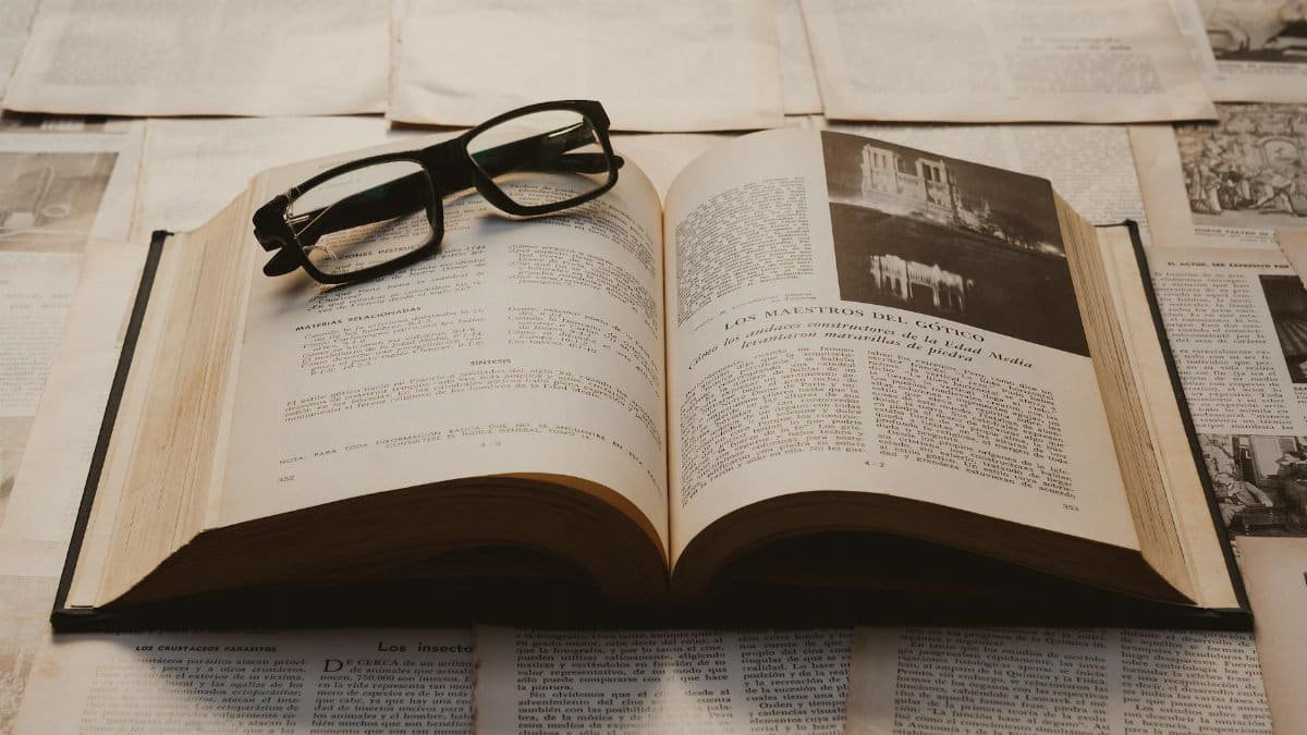 A vintage book open on a table, surrounded by old papers, with resting glasses.