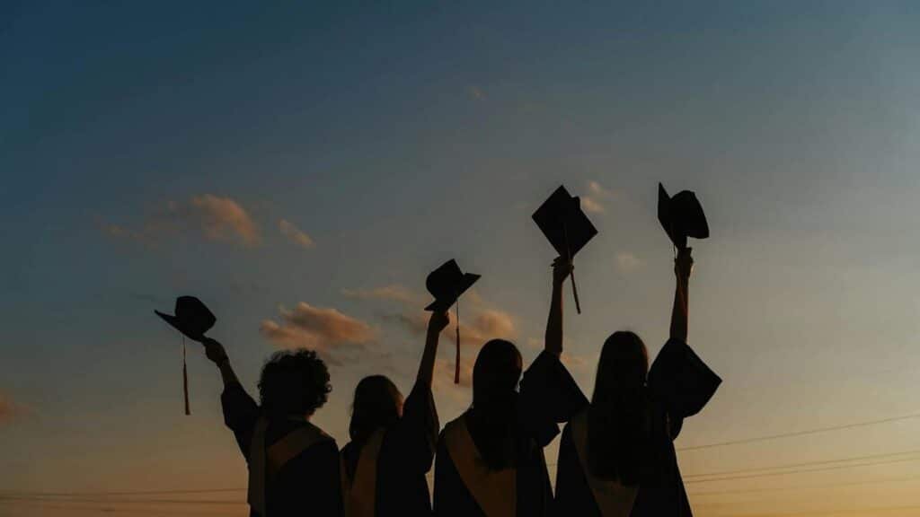 A group of graduates celebrate by raising their caps against a vibrant sunset sky, symbolizing achievement.