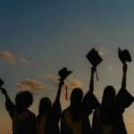 A group of graduates celebrate by raising their caps against a vibrant sunset sky, symbolizing achievement.
