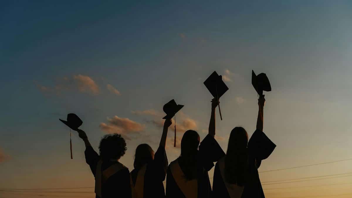 A group of graduates celebrate by raising their caps against a vibrant sunset sky, symbolizing achievement.