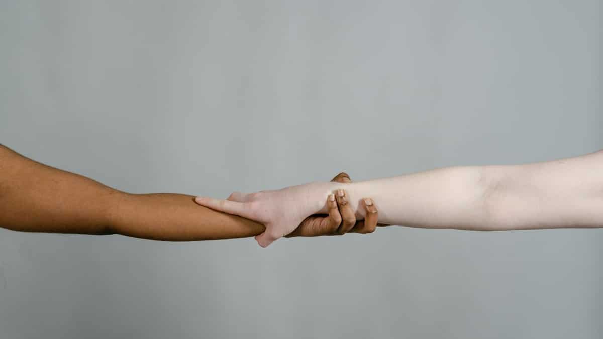 Close-up of two diverse hands reaching towards each other on a plain background, symbolizing unity.