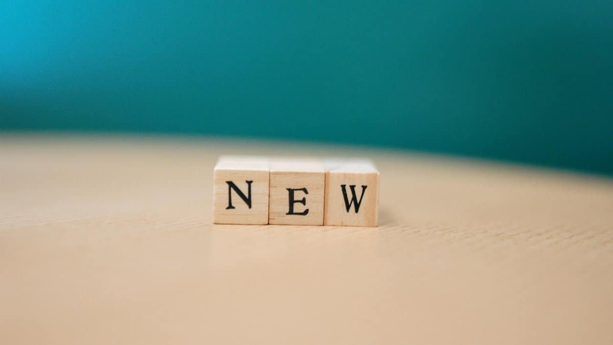 Wooden blocks spelling out 'NEW' on a wooden surface against a teal background.