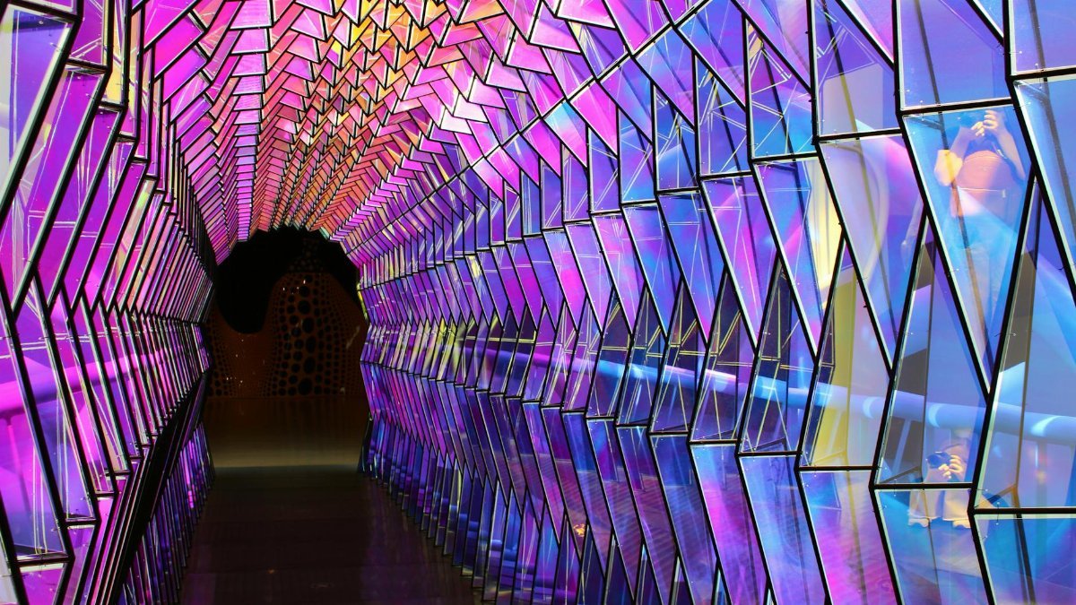 A colorful geometric tunnel featuring reflective and illuminated panels at a San Francisco exhibition.