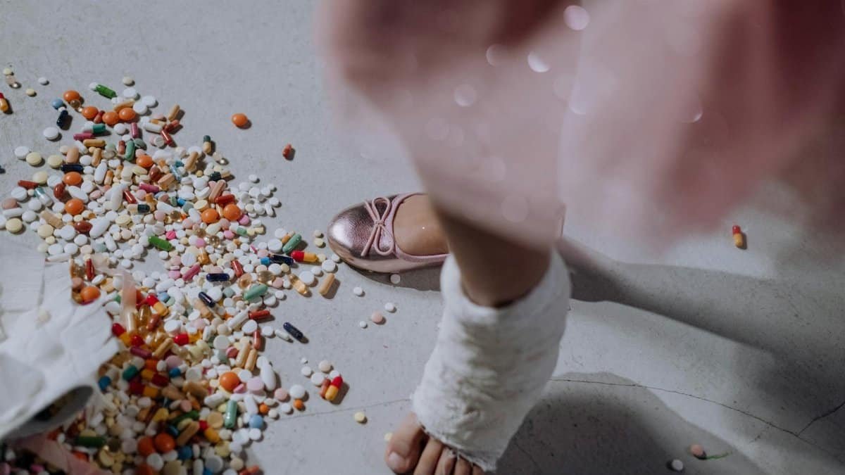 A child's foot in a cast next to a pile of scattered pills on a white floor.