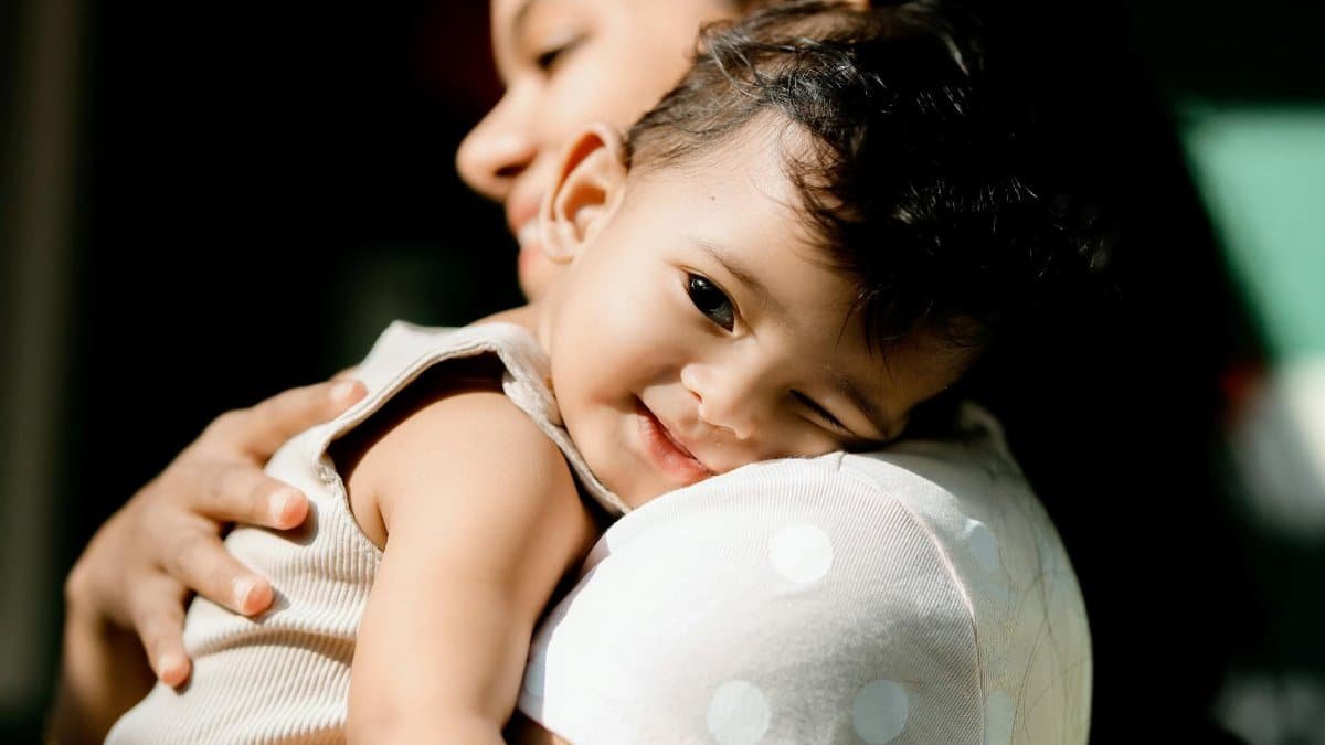 A mother lovingly holds her smiling baby, showing affection and bond in a tender moment.