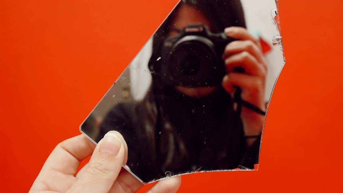 A creative self-portrait captured through a broken mirror against a vivid red background.