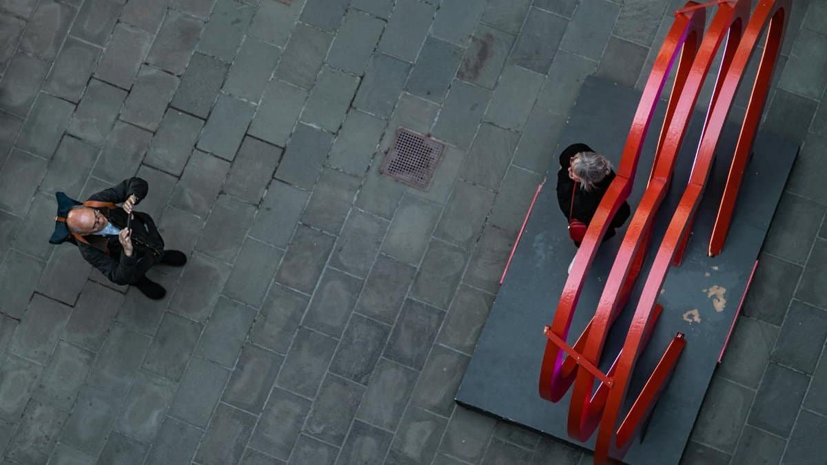 Top view of a man photographing a woman near a red abstract sculpture.