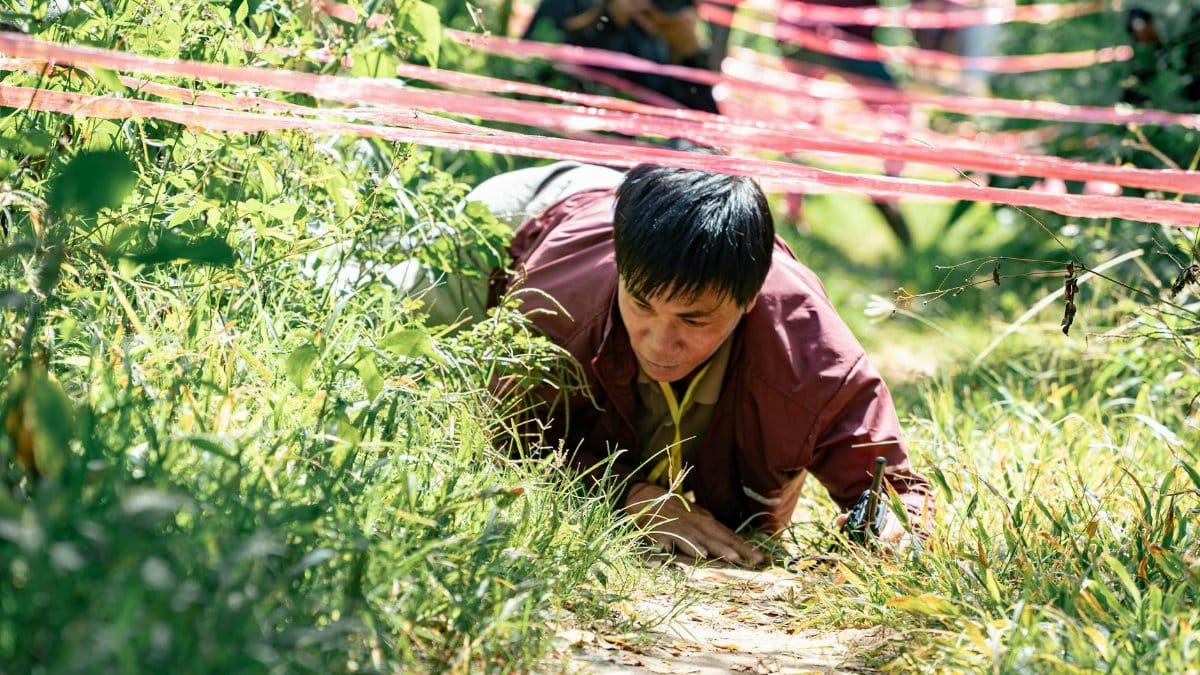 A man crawls under ropes in an outdoor obstacle course challenge.