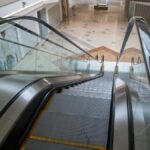 An escalator inside a deserted shopping mall with closed storefronts and empty spaces, capturing urban decay.