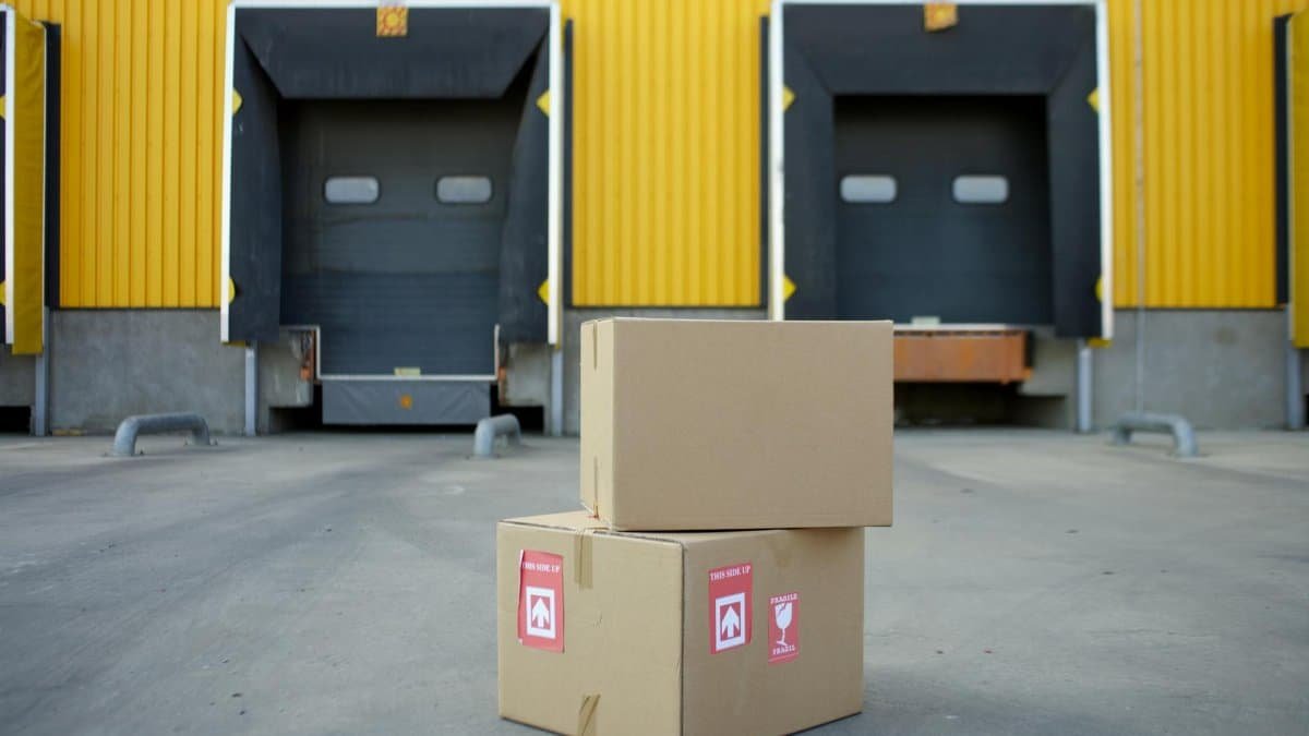 Cardboard boxes stacked in front of industrial warehouse loading docks with yellow walls.