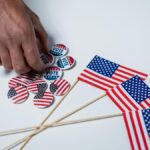 A hand reaches for voting buttons and American flags on a white background.