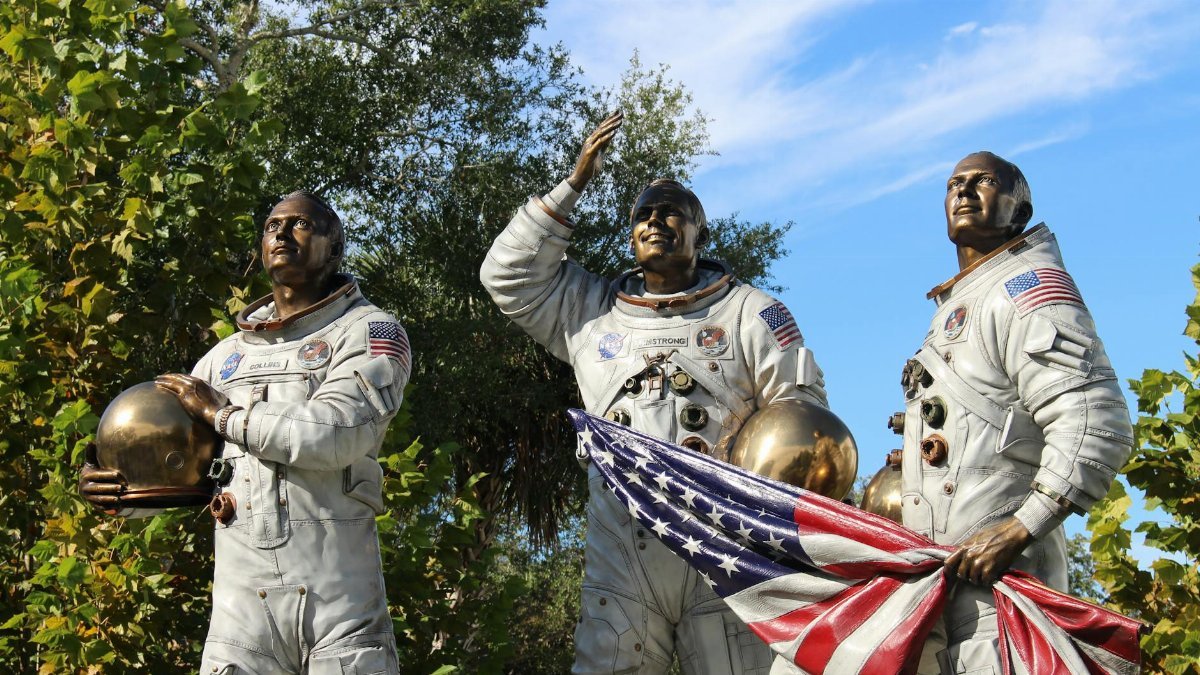 Bronze statue of Apollo astronauts at Cape Canaveral, holding a flag.