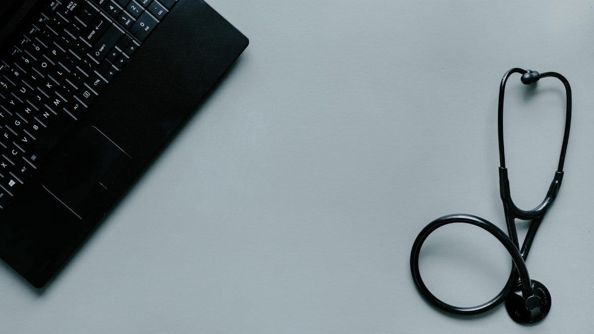 Minimalist image depicting a laptop and stethoscope representing telemedicine and digital health.