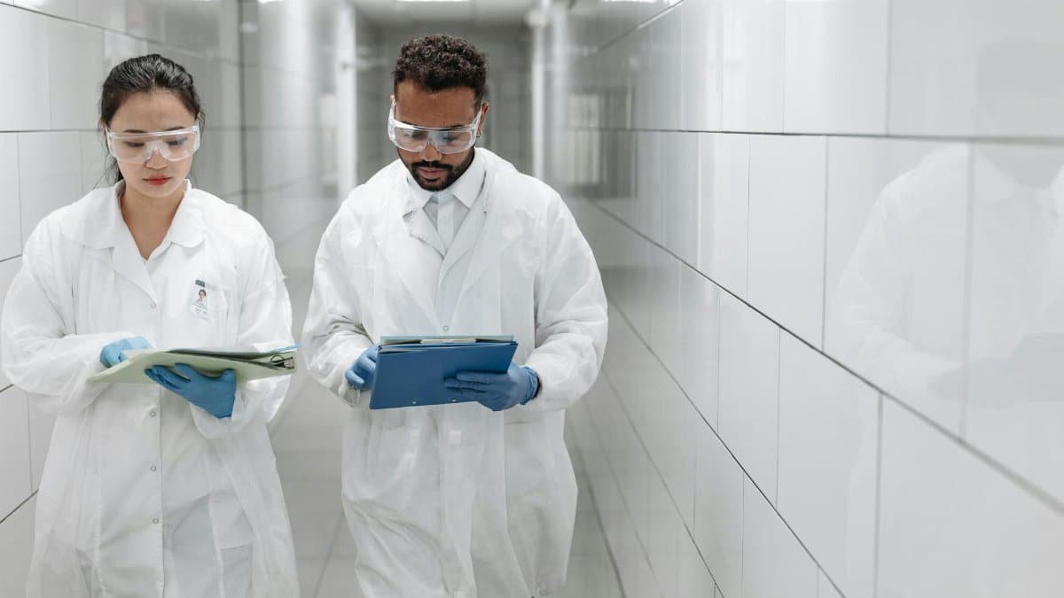 Two researchers in lab coats review documents in a clinical laboratory hallway.
