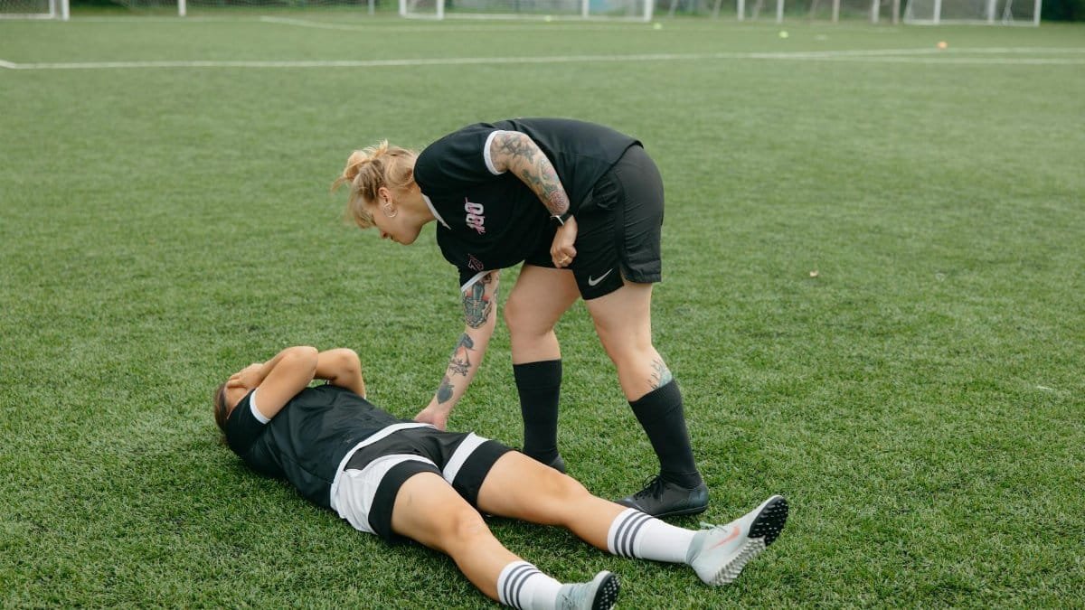 A female soccer player helps an injured teammate on a green soccer field during a game.