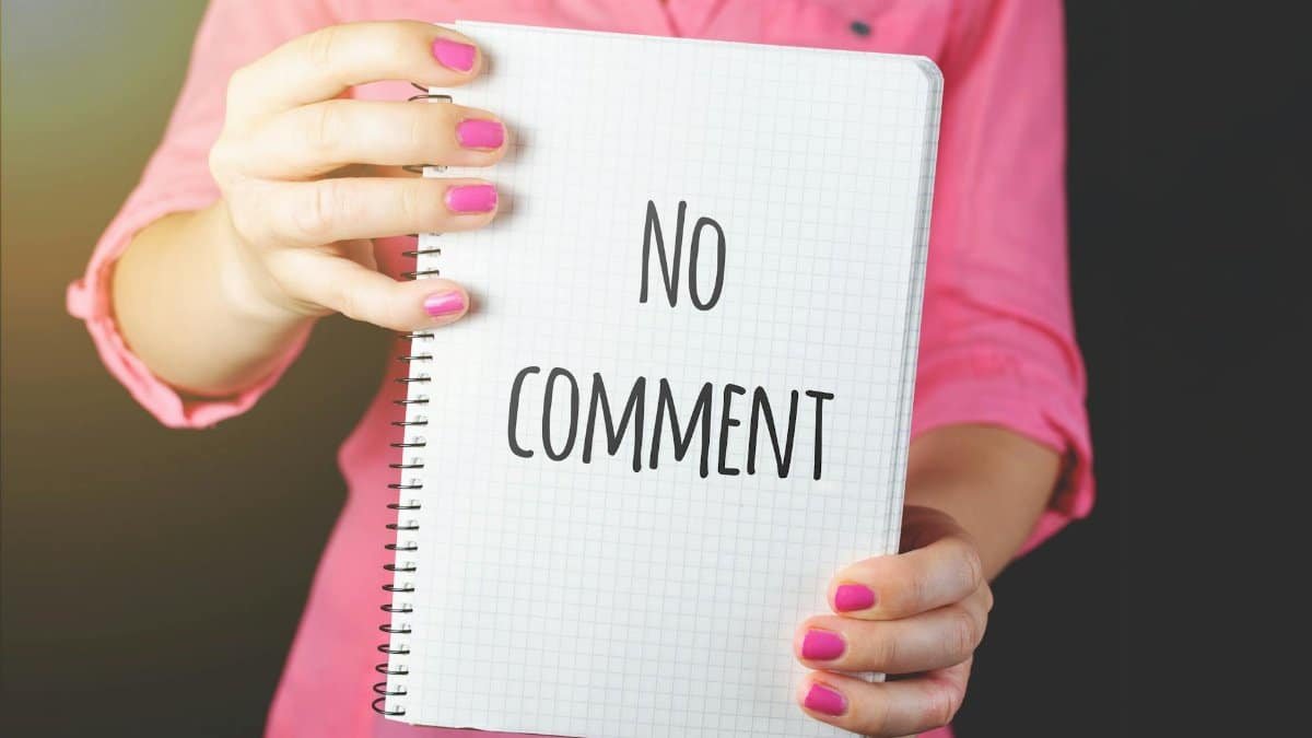 A woman in a pink shirt holds a notebook with 'No comment' text visible, conveying silence or privacy.