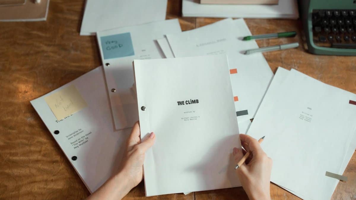 Close-up of hands holding script pages on a wooden desk with a typewriter.