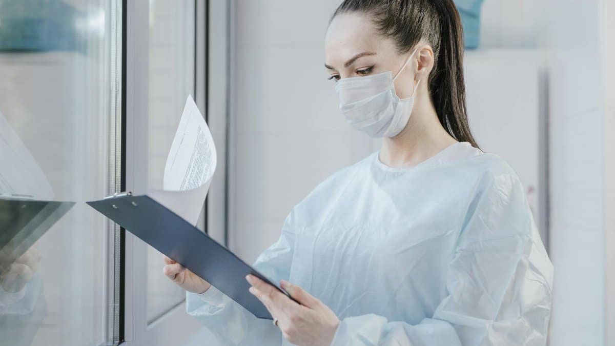 A female doctor in a mask examining patient's medical records in a hospital setting.