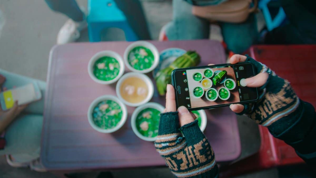 A person photographing vibrant green street food bowls with a smartphone.