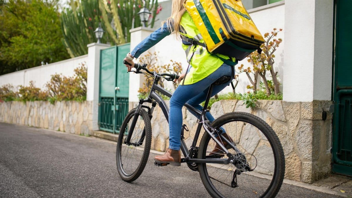 A female courier riding a bicycle for food delivery on a street in Portugal.