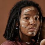 A woman holds a broken mirror with positive messages on her face, reflecting self-acceptance.