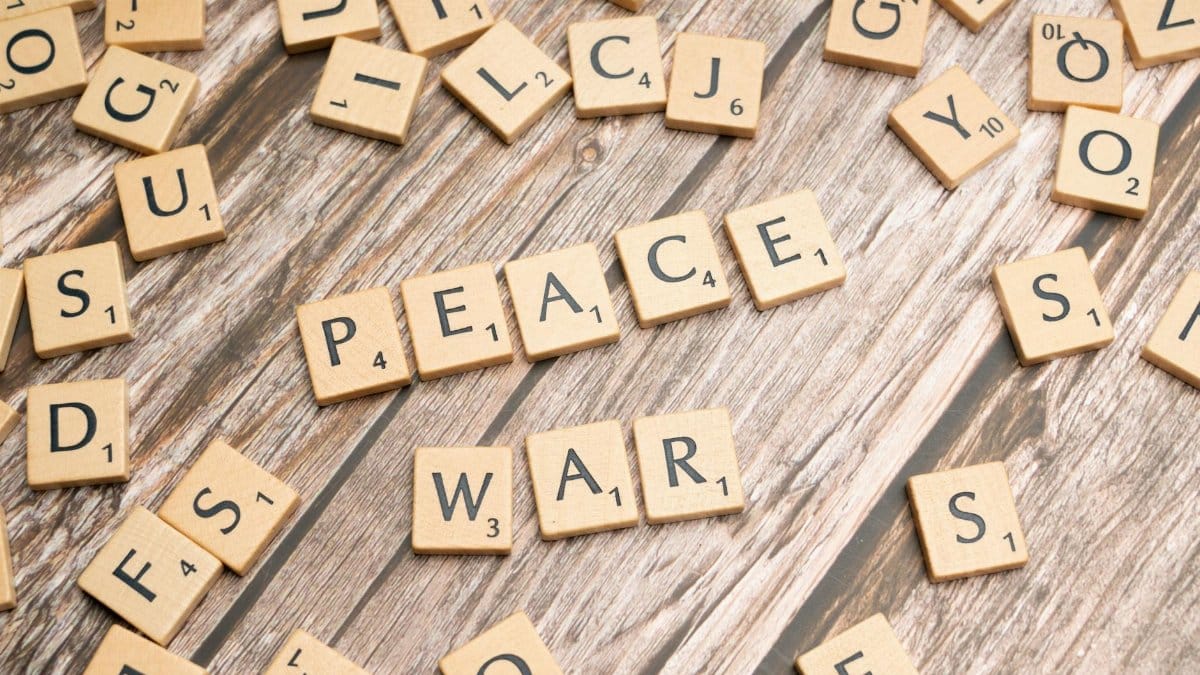 Wooden letter tiles spelling 'PEACE' and 'WAR' on a rustic surface.