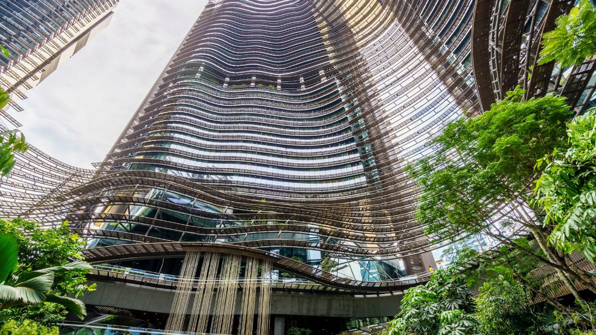 Stunning modern skyscraper with an architectural wave facade and lush greenery in an urban setting.