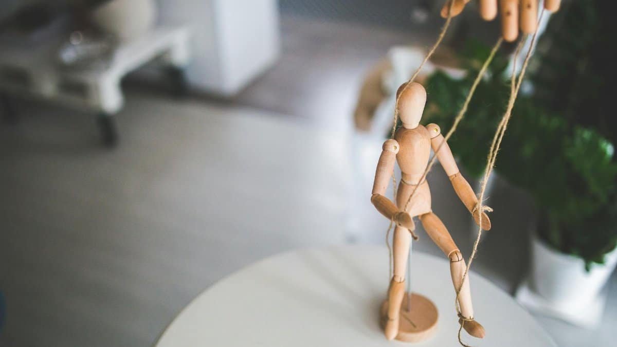 Close-up of a wooden marionette controlled by strings indoors. Artistic representation of control and manipulation.