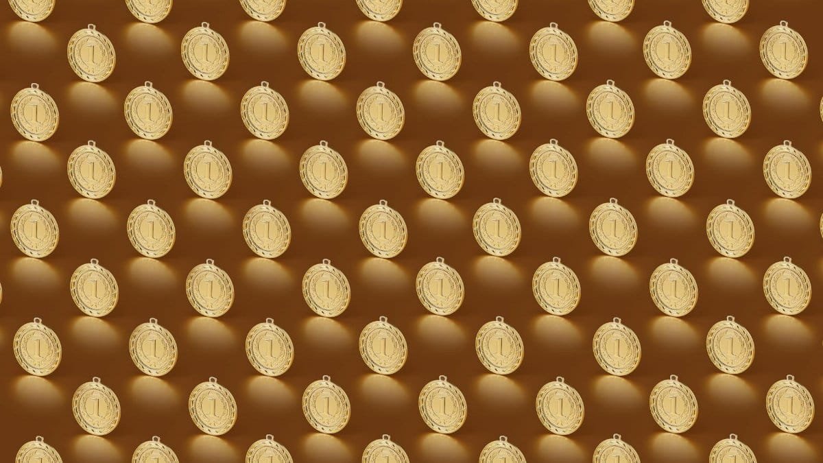 Multiple gold medals arranged in a repeating pattern on a brown backdrop.