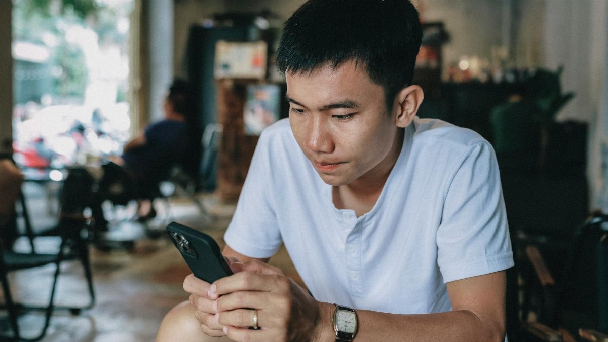 Casually dressed young man engaged with his smartphone, seated indoors.