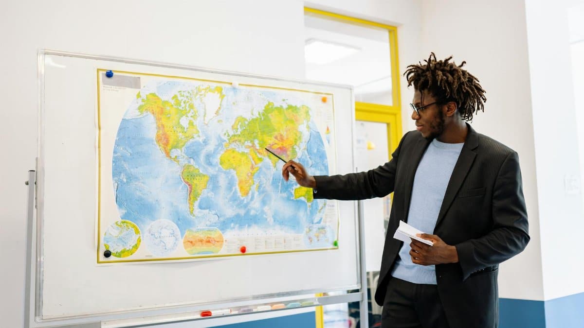 Teacher pointing at world map during classroom lesson, engaging students.