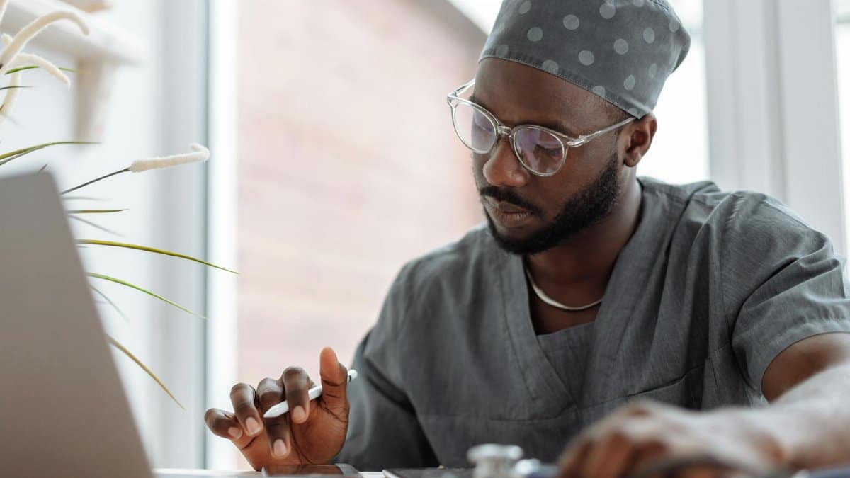 A focused male doctor in scrubs working on a laptop, showcasing professionalism and modern healthcare technology.