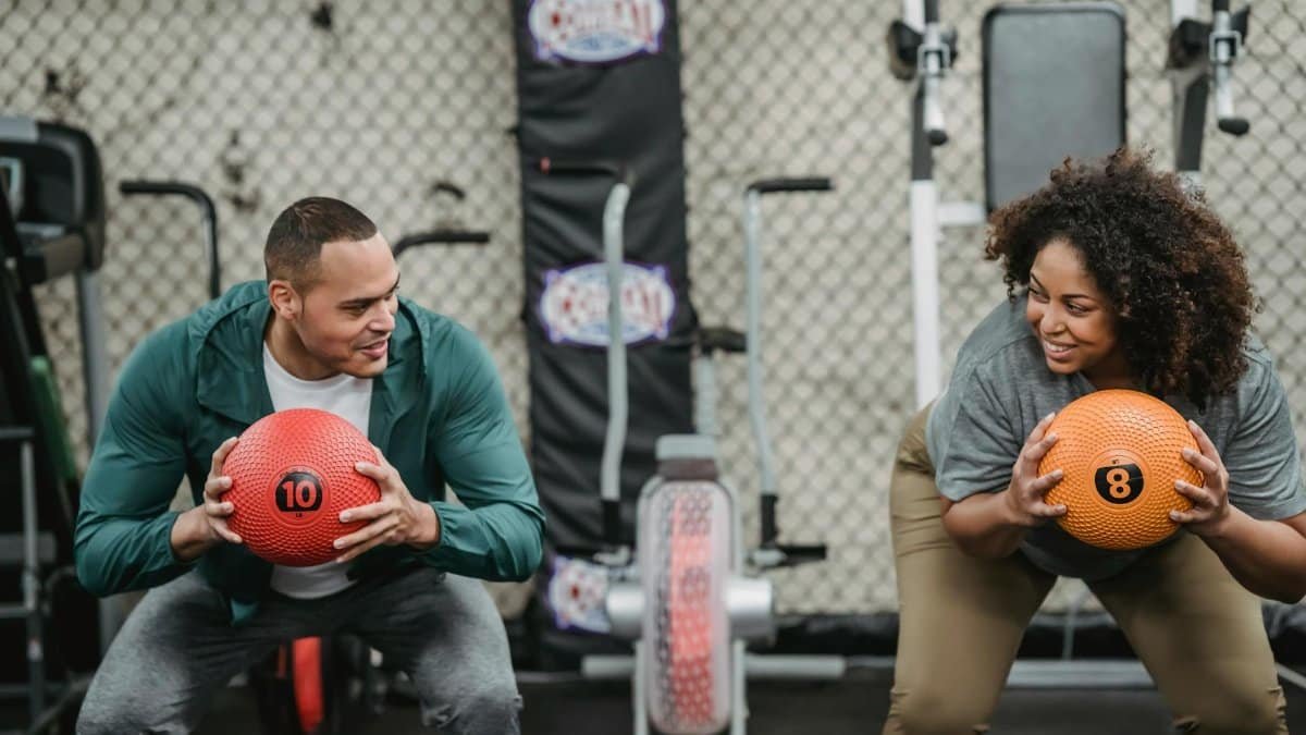 Diverse man and plump woman exercising with bright balls in sport club with gym equipment
