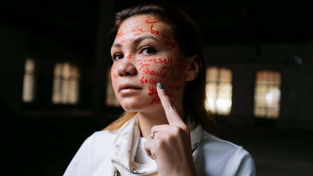 A woman with words written on her face poses in an artistic expression of activism and self-identity.