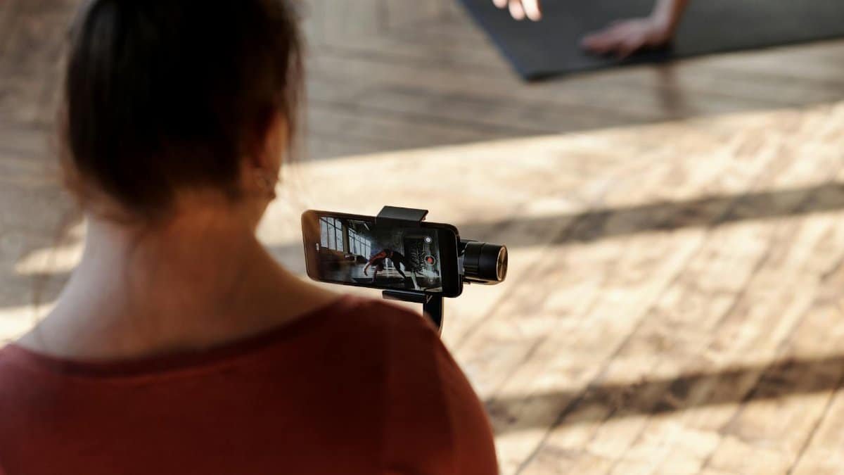 Woman recording a yoga session indoors using a smartphone on a stand, with focus on technology and fitness.