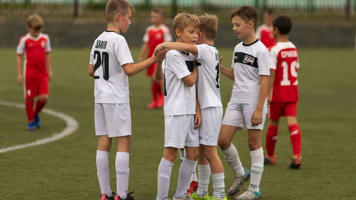 Youth soccer players huddle in sports uniforms on a grass field, fostering teamwork and unity.
