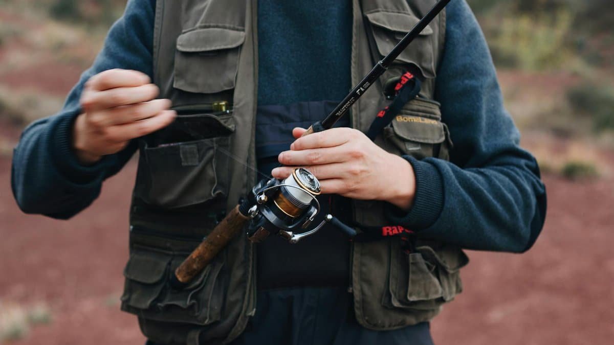 Close-up of a man holding a fishing rod, adjusting the line outdoors.
