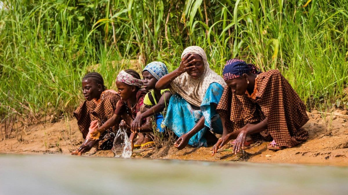 Group of children sitting by a riverbank, enjoying a sunny day outdoors.