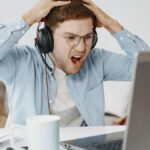 Man experiencing frustration at home office while working on laptop.
